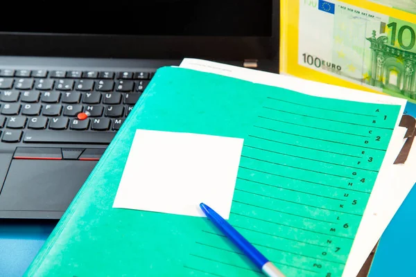 Laptop keyboard and green Folder with empty sticky note message, paper note and 100 Euro paper currency