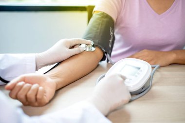 Doktor, hastayı steteskopla, tansiyon monitörüyle muayene eder ve sonuçları kaydeder..