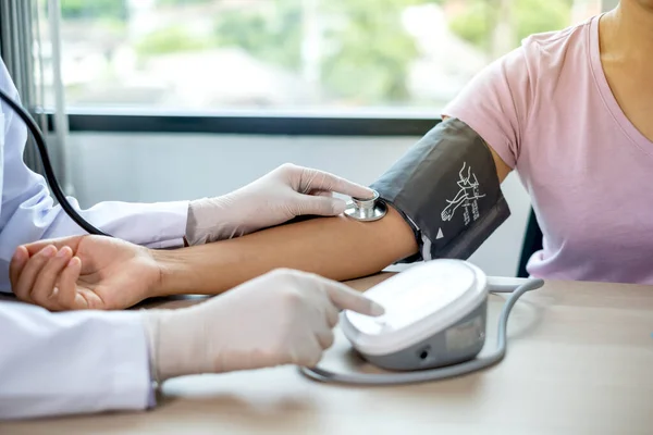 Doktor, hastayı steteskopla, tansiyon monitörüyle muayene eder ve sonuçları kaydeder..