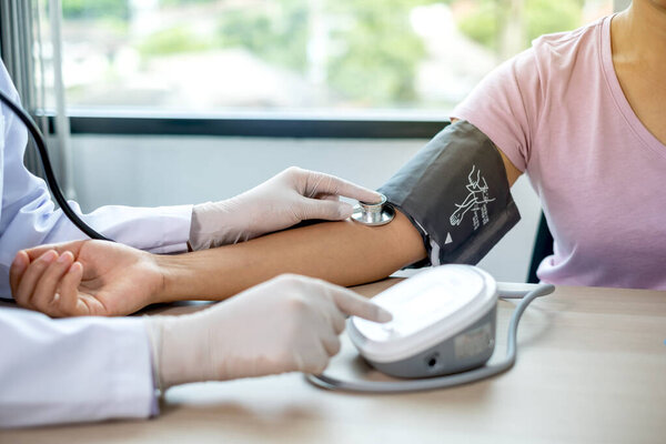 Doctor evaluates the patient with a stethoscope, blood pressure monitor and records the results.