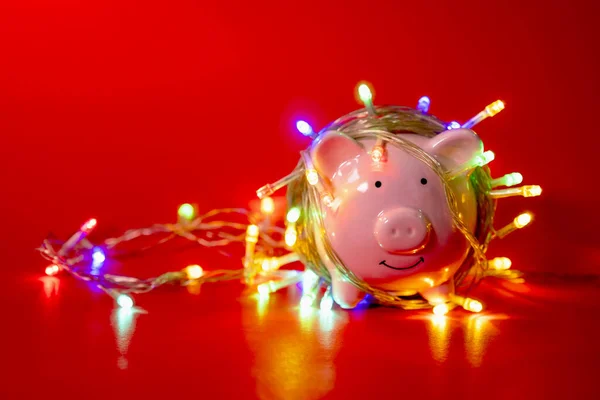 Kırmızı arka planda mutlu aralık festivalinde Noel telli ışıkları olan pembe kumbaralar tatil konseptine para harcamak için tasarrufların tadını çıkarın..