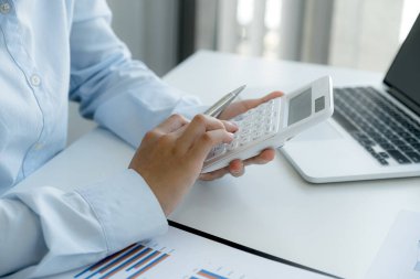 İş kadınları muhasebecisi, çalışma odasındaki beyaz masada vergi ödemeyi hesaplayan hesap makinesi ve dizüstü bilgisayar kullanır.