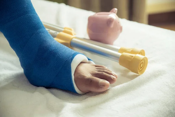 Adamın bacağı ameliyat sonrası yürümek için koltuk değneği kullanıyor. Kırık kemikler ve domuz kumbarası..