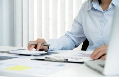 İş kadını el çabukluğu ile hesap makinesi kullanır ve merkez ofisteki bilgisayarla grafiği analiz eder. İş hedeflerini belirler ve yeni hedefe ulaşmayı planlar..