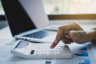 İş kadınları muhasebecisi el bilgisayarı ve hesap makinesi kullanır. Çalışma odasındaki beyaz masanın üzerindeki vergiyi hesaplar..