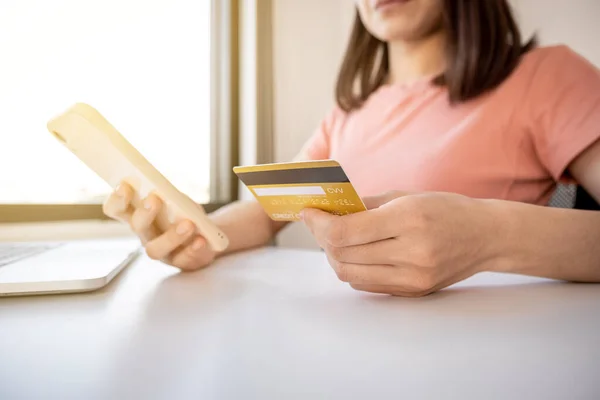 Young Asian consumer woman hand holding a credit card, Ready to spending pay online shopping according to discount products via smartphone and laptop from home.