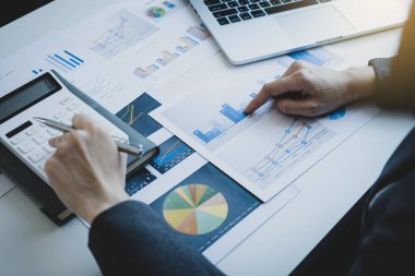 İş kadınları muhasebecisi grafiğe işaret ediyor. Çalışma odasındaki beyaz masada vergi ödemeyi hesaplayan hesap makinesi ve dizüstü bilgisayar kullanıyor..