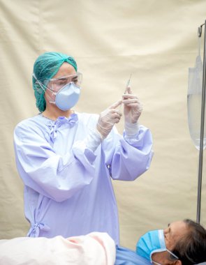 Doktor yaşlı hastalara enjeksiyon hazırlıyor. İkisi de COVID salgını yüzünden maske takıyordu..