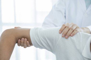 Kadın doktor, erkek bir hastanın omzunu uzatarak fizik tedavi uyguluyor..