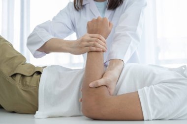 Kadın doktor elleri, erkek bir hastanın kolunu uzatarak fizik tedavi uyguluyor..