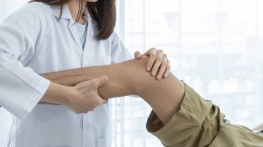 Kadın doktor elleri, erkek bir hastanın bacağını ve dizini uzatarak fizik tedavi uyguluyor..