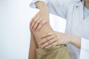 Kadın doktor elleri, erkek bir hastanın bacağını ve dizini uzatarak fizik tedavi uyguluyor..