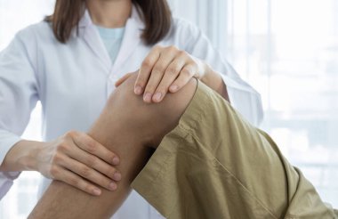 Kadın doktor elleri, erkek bir hastanın bacağını ve dizini uzatarak fizik tedavi uyguluyor..