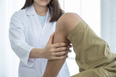 Kadın doktor elleri, erkek bir hastanın bacağını ve dizini uzatarak fizik tedavi uyguluyor..