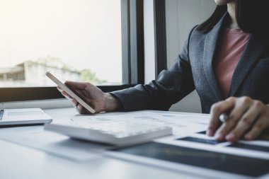 İş kadınları muhasebecisinin elinde akıllı telefon ve çalışma odasındaki beyaz masanın vergilerini ödemesi için dizüstü bilgisayar kullanımı.