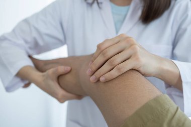 Kadın doktor elleri, erkek bir hastanın bacağını ve dizini uzatarak fizik tedavi uyguluyor..