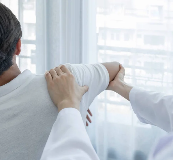 Kadın doktor, erkek bir hastanın omzunu uzatarak fizik tedavi uyguluyor..