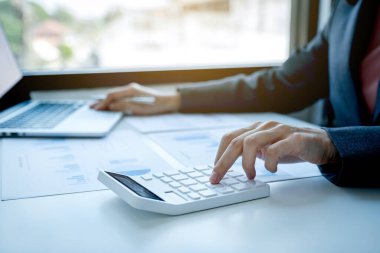 İş kadınları muhasebecisi el bilgisayarı ve hesap makinesi kullanır. Çalışma odasındaki beyaz masanın üzerindeki vergiyi hesaplar..