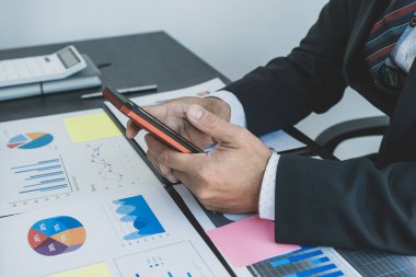 İşadamı, işletme işletme hedeflerini belirlemek ve yeni hedefine ulaşmayı planlamak için ofisteki akıllı telefonla finans grafiğini analiz ediyor.