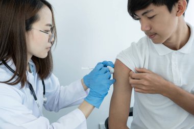 Doktor elinde bir şırınga tutuyor ve virüsün yayılmasını önlemek için klinikte bir hastaya aşı yapmak üzereydi..