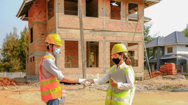 Mühendis müteahhit ekibi iş güvenliği planı projesiyle tanıştıktan sonra el sıkışıyor ve inşaat alanında tasarımı kontrol ediyor..