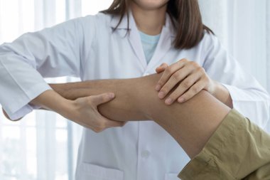 Kadın doktor elleri, erkek bir hastanın bacağını ve dizini uzatarak fizik tedavi uyguluyor..