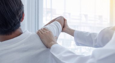 Kadın doktor, erkek bir hastanın omzunu uzatarak fizik tedavi uyguluyor..