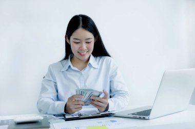Uzun saçlı, güzel bir Asyalı kadın bir dolar tutuyor. İç işlerinde çalışan beyaz masa üzerinde vergi ödeyen bir dizüstü bilgisayar kullanıyor..