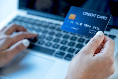 Tüketici kadın elinde sahte bir kredi kartıyla ev ofisinden gelen dizüstü bilgisayarla indirimli ürünlere göre online finans alışverişi yapmaya hazır..