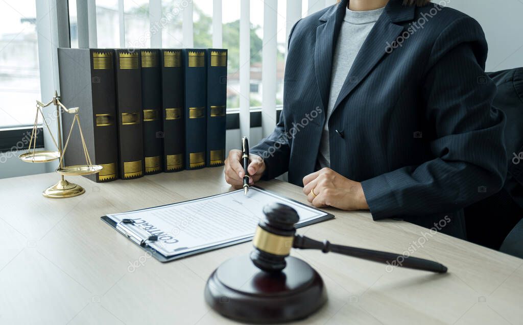 The woman lawyer is sitting at the desk in the office with a justice scale and gavel hammer. Study the law in business disputes to give advice to customers.