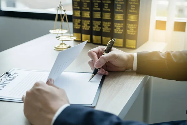 Lawyer hand holding pen and providing legal consult business dispute service at the office with justice scale and gavel hammer.