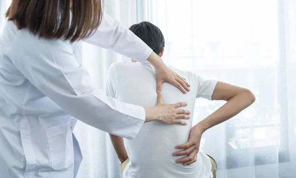 Kadın doktor elleri, erkek bir hastanın sırtını uzatarak fizik tedavi uyguluyor..