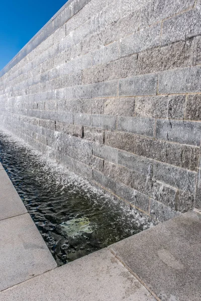 Şelale özellikli uzun taş bir duvar. Yandan bir havuza sıçrıyor. Güneşli bir günde, arka plan ve fotokopi alanında suyun tekrar tekrar aktığı bir yer.