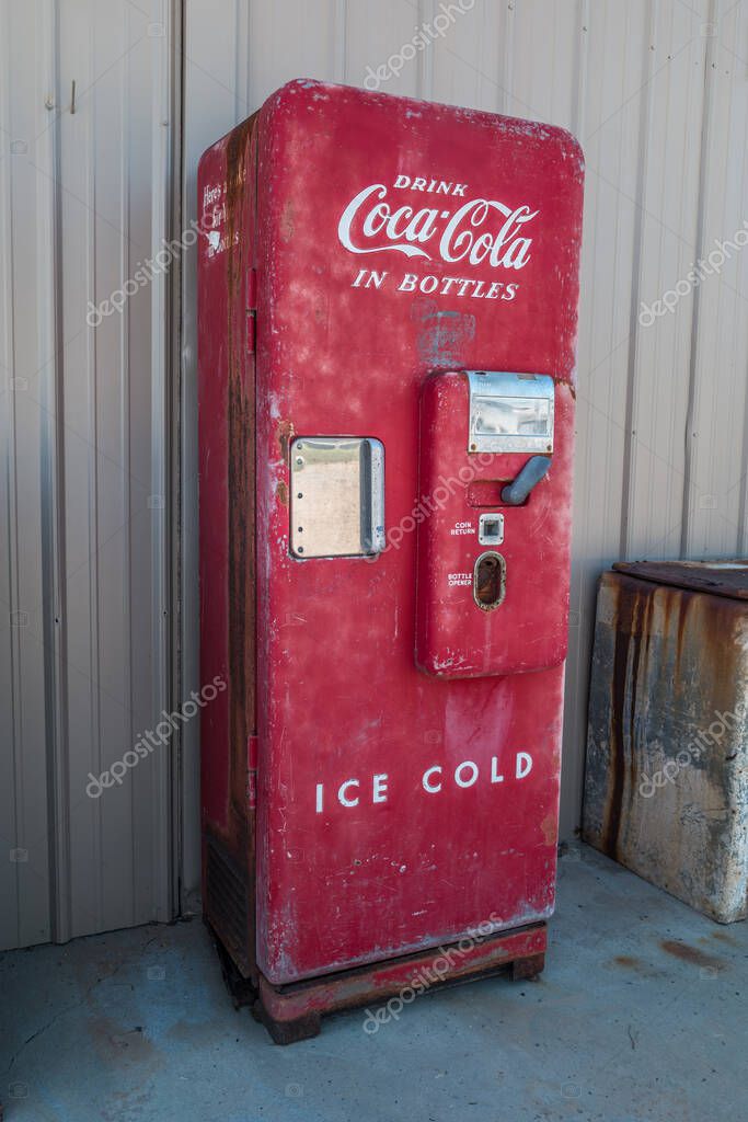 Gainesville, Georgia USA - June 13, 2020  A bright red vintage Coca-Cola vending machine intact with original parts and some patina standing vertical outdoors against a building