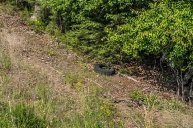 Tepenin yamacında dikilip yolun kenarındaki bir hendeğe atılmış kullanılmış bir lastiğe bakarken güneşli bir günde diğer enkazlar etrafını sarmış.