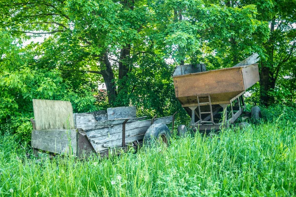夏天阳光灿烂的日子里 几辆锈迹斑斑 风风吹日晒的旧货车将废弃的农机具倾倒在一片繁茂的农田里 — 图库照片