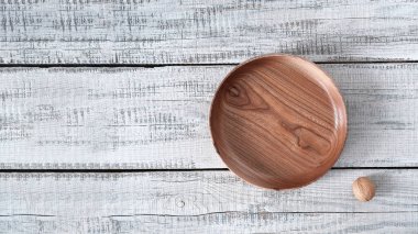 Ahşap bir arka planda, karaağaçtan yapılmış bir tabak ve yanında bir ceviz.