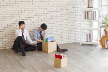 İki erkek çalışan, işten kovulduktan sonra ellerinde kişisel kullanım için bir karton kutuyla yerde oturmuş birbirleriyle konuşuyorlardı..