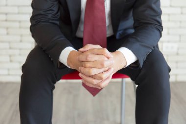 Takım elbiseli Asyalı bir adam, oturuyor, el ele tutuşuyor, zihnini sandalyede sakinleştiriyor.