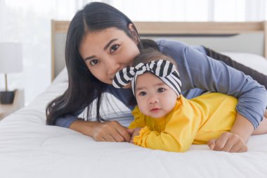 Asyalı bir anne bebeğiyle yatakta sevgi ve özenle oynar..