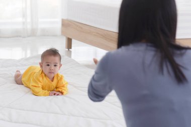 Annesiyle birlikte yatak odasındaki yumuşak beyaz bezinin diğer tarafında sürünen Asyalı bir bebek.