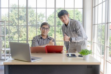 Oğlu ofiste bir masanın yanında duran Asyalı orta yaşlı bir adam..