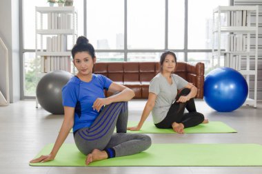 İki orta yaşlı Asyalı kadın evinde lastik bir paspasın üzerinde yoga yapıyor..