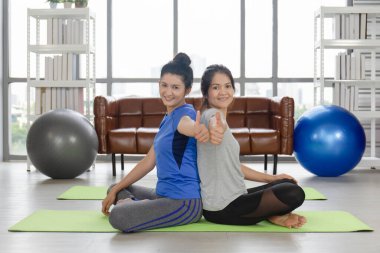 İki orta yaşlı Asyalı kadın, evinde kauçuk bir paspasın üzerinde başparmaklarını kaldırmış, harika bir duygu ifade ediyorlar..