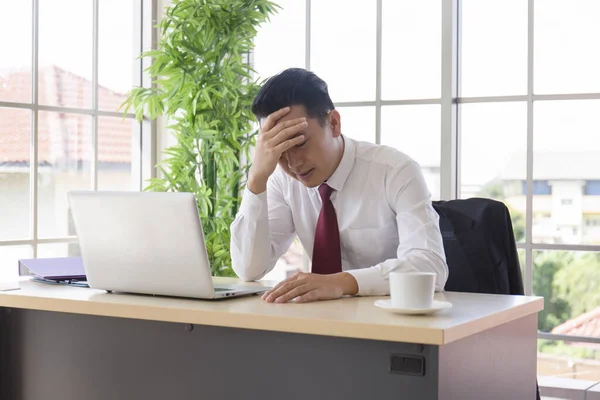 An Asian man manager is stressed out in the office after a sharp drop in corporate revenues.