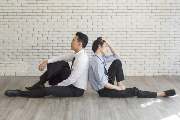 Two male employees sat on the floor showing signs of stress from overwork.