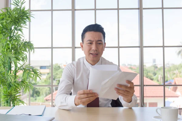 A man in an Asian company receives important documents on his desk with a shocked expression.