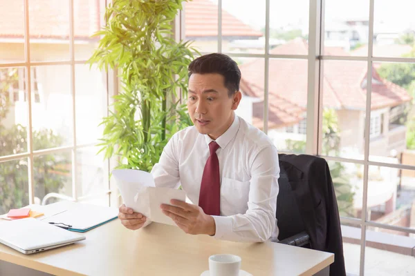 アジアの企業の男性はショックを受けた表情で彼の机の上に重要な文書を受け取ります — ストック写真
