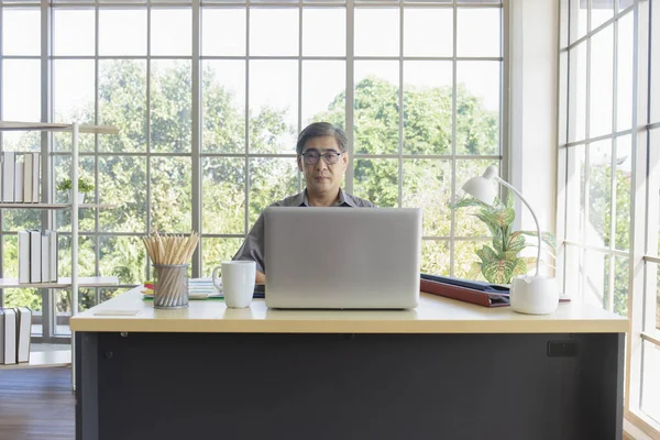 オフィスの机に座っているアジア系の中年男性 — ストック写真