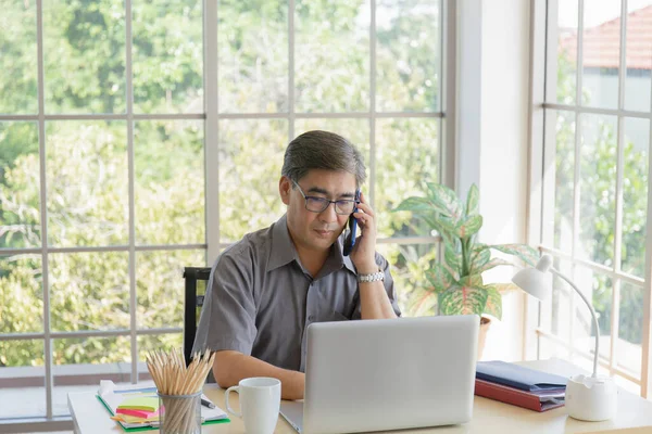 Азиатский Мужчина Среднего Возраста Разговаривает Телефону Своим Столом Офисе — стоковое фото